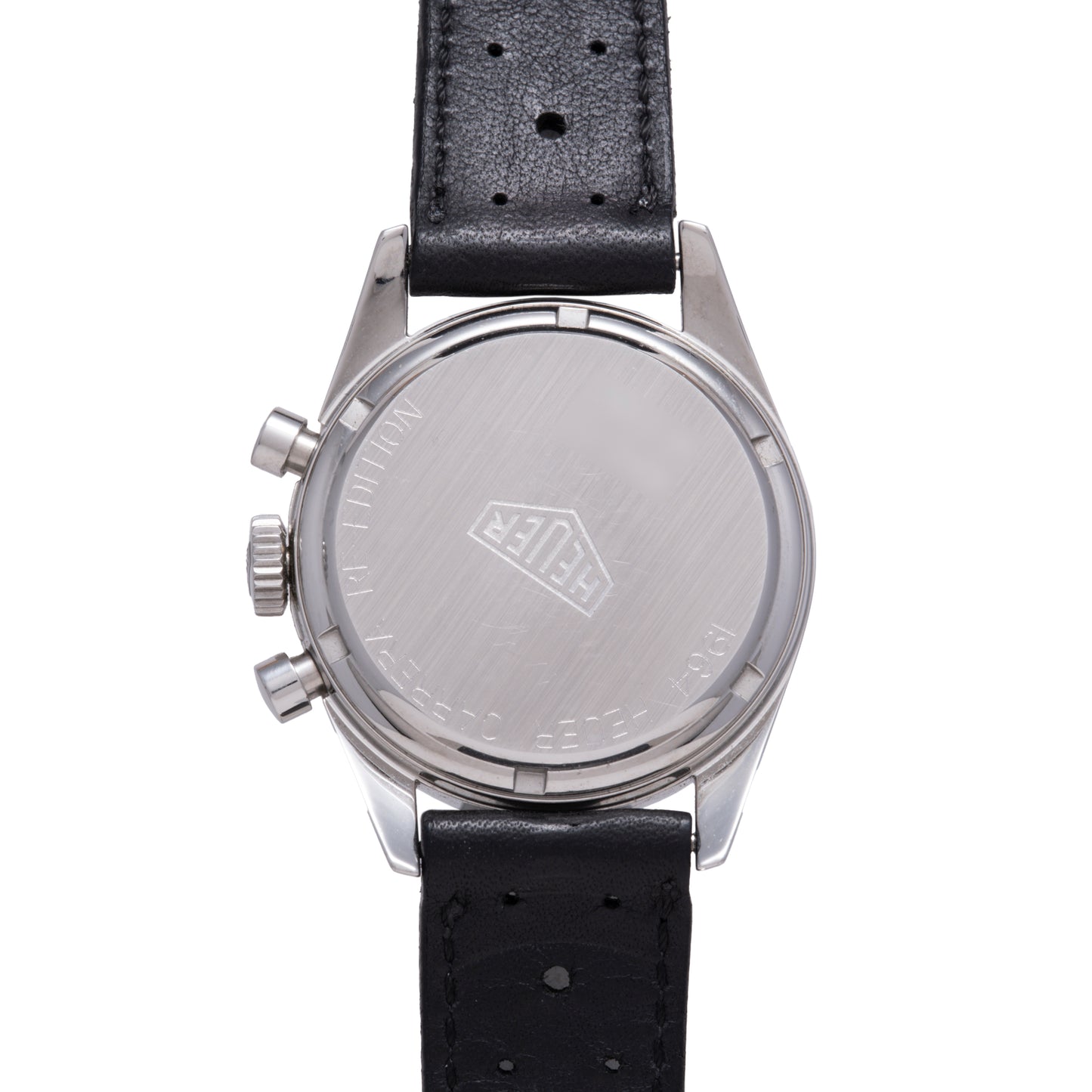 The back of the TAG Heuer 1964 Carrera Re-Edition shows a brushed metal case with engraved logo and black perforated leather strap. Two crown buttons are visible on the side of this vintage TAG Heuer chronograph.