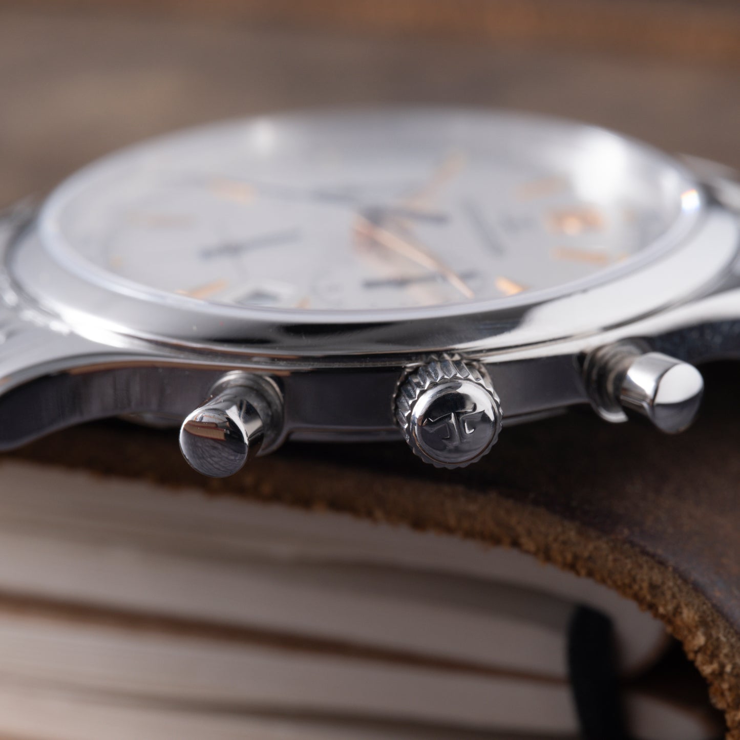 Side view of the Jaeger-LeCoultre Master Control Chronograph Mecaquartz, with pushers and crown visible as it rests on a brown leather book, emphasizing Jaeger LeCoultre’s signature Mecaquartz precision and Calibre 630 details.