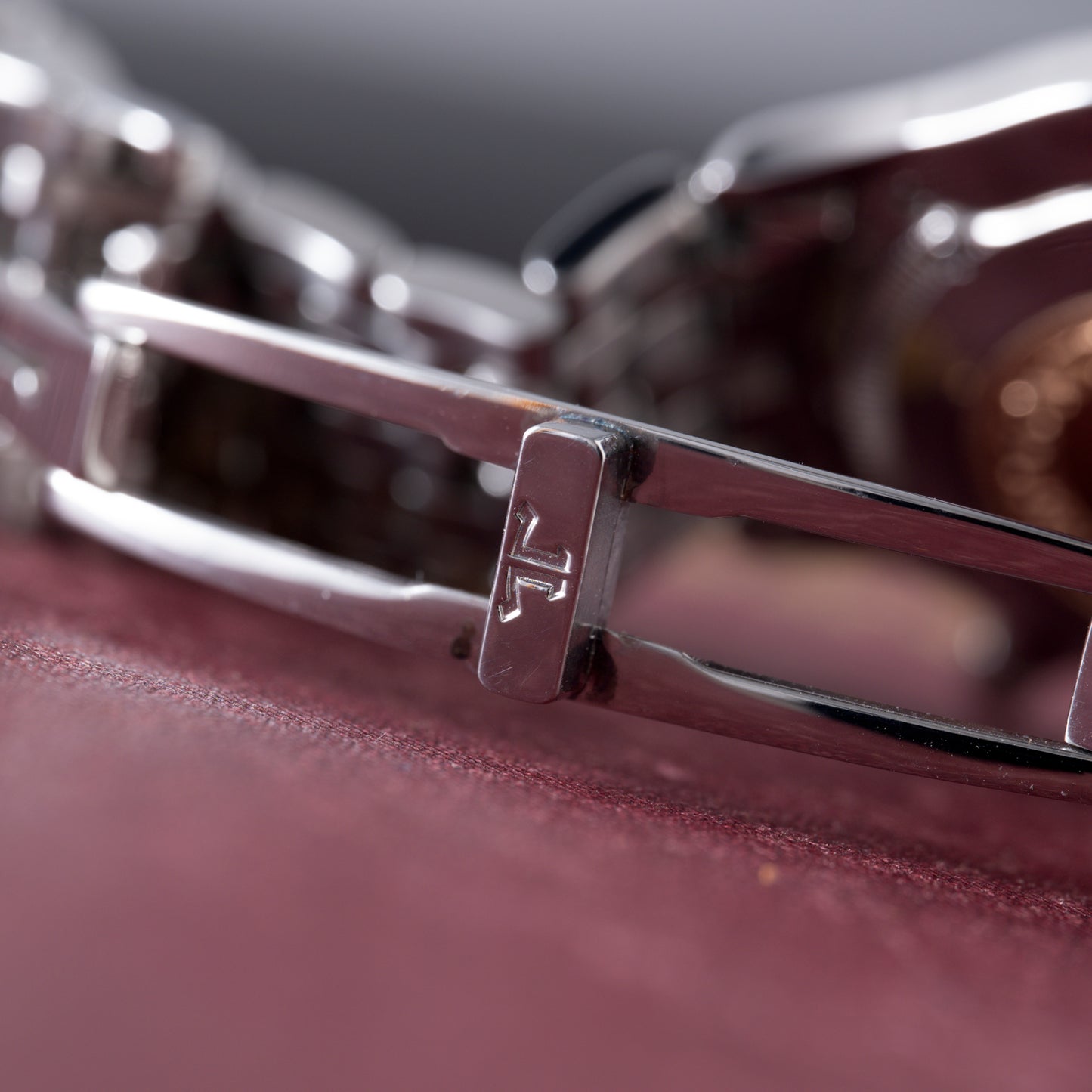 Close-up of a Jaeger-LeCoultre Master Control Chronograph Mecaquartz silver bracelet with engraved JL initials on the clasp, resting on burgundy. The shot emphasizes the shiny reflective metal links and fine craftsmanship.