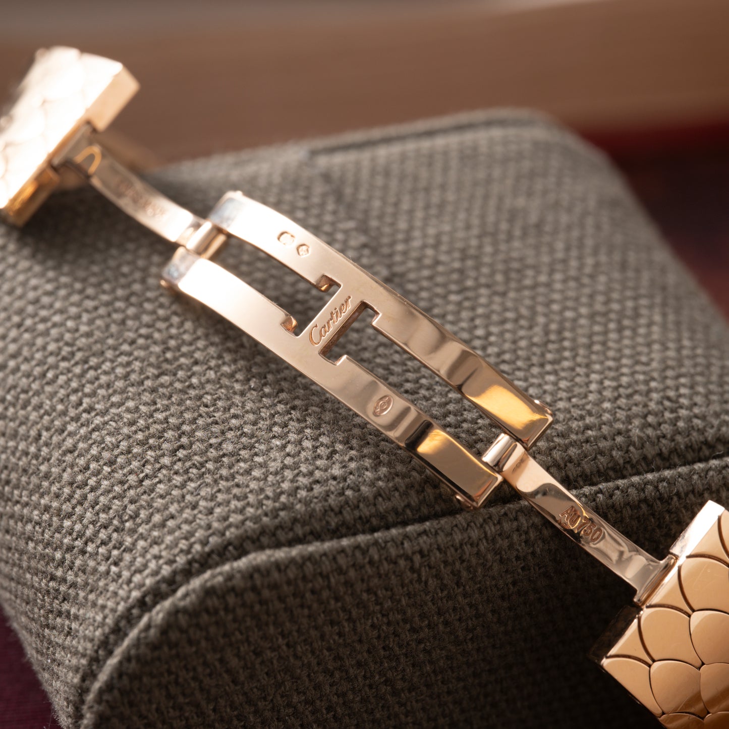 Close-up of a Cartier Tank Americaine Automatic Diamonds clasp in polished 18K rose gold, engraved with Cartier branding and visible hallmarks, displayed open on a textured dark gray fabric cushion.