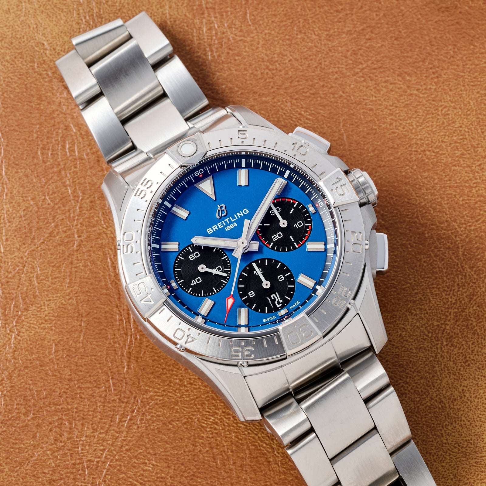 The Breitling Avenger B01 Chronograph 42 is a stainless steel aviation watch with a blue dial, three black subdials, red and white hands, metal bracelet, and COSC-certified automatic movement, shown on brown leather.