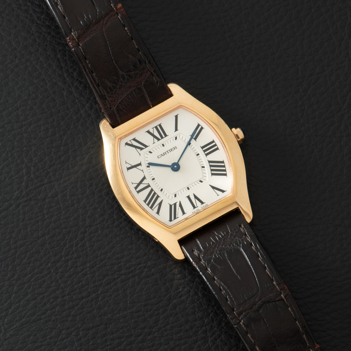 Gold-tone Cartier Tortue watch with cream dial, Roman numerals, and dark brown leather strap.