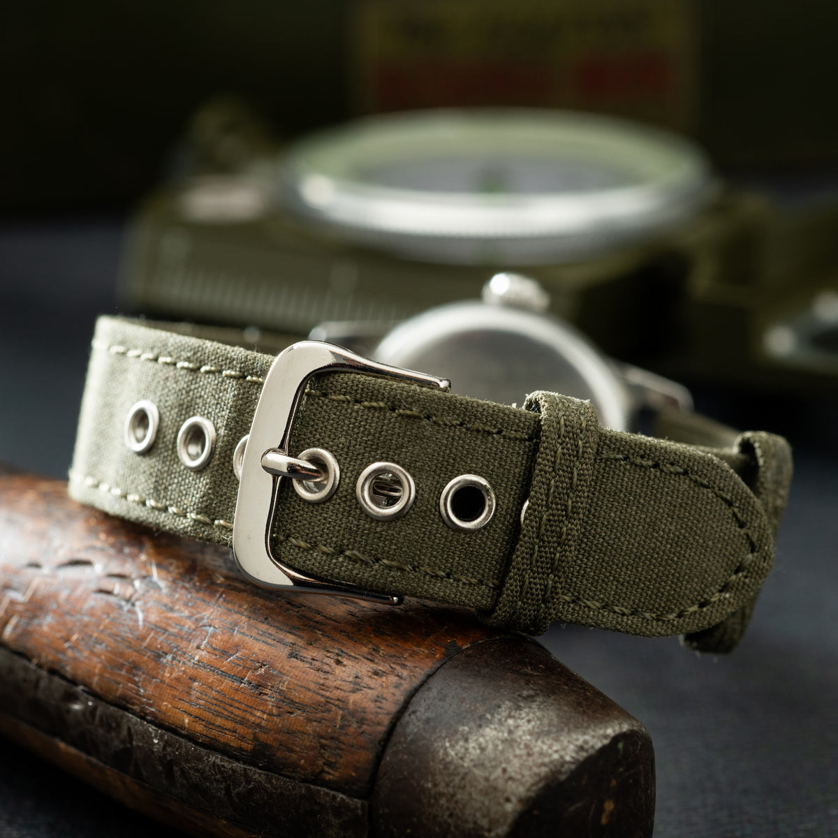 Waltham A-17 military watch with olive canvas strap and metal buckle on wooden surface.