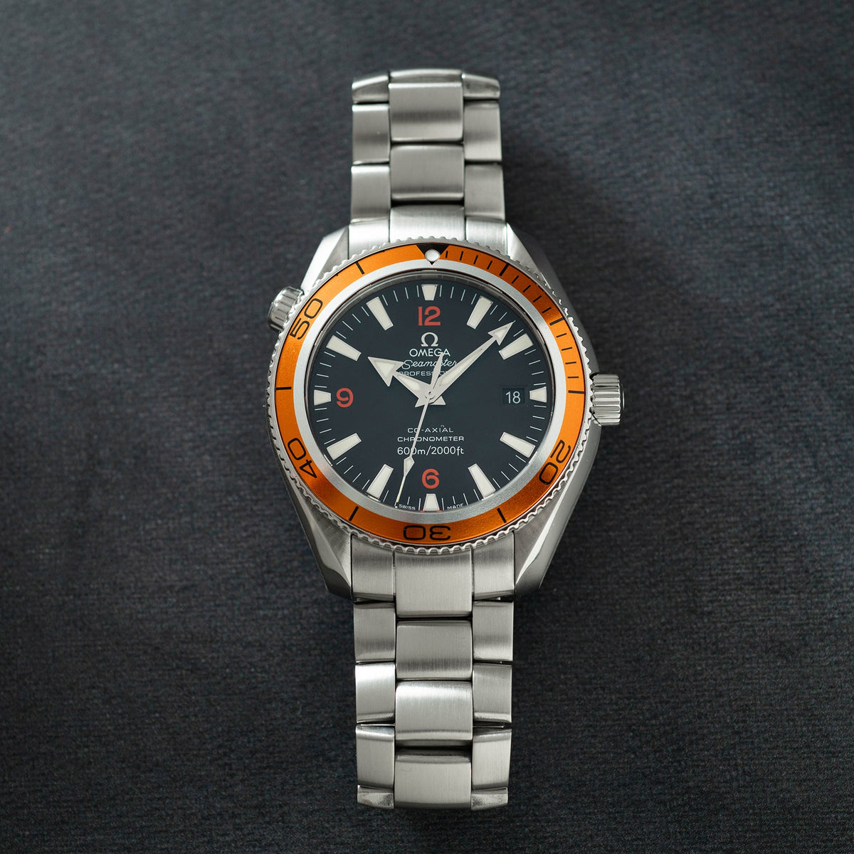Silver stainless steel watch with black dial, orange bezel, and matching bracelet displayed against gray background.