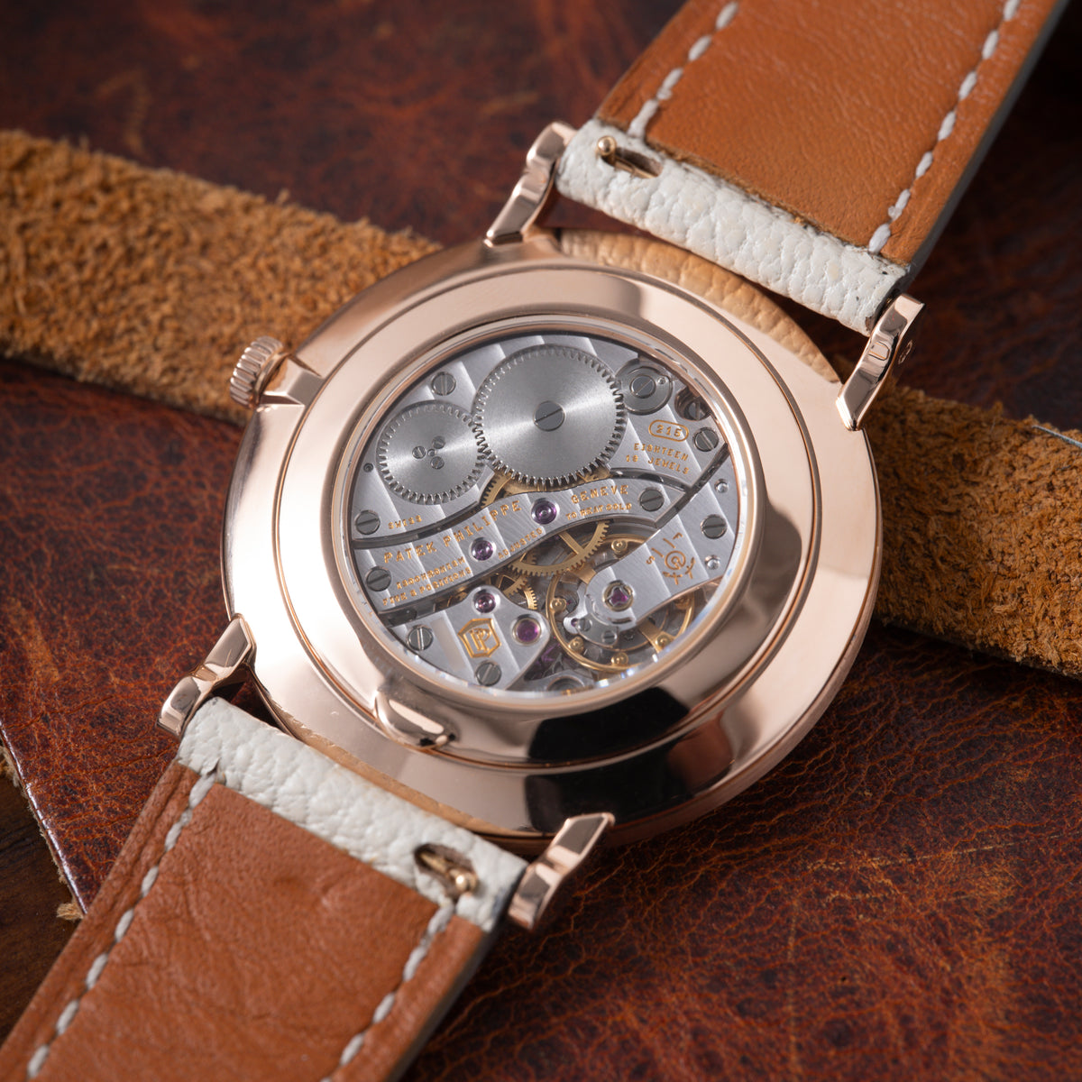 Rose gold watch with skeletonized dial showing visible gears and jewels, paired with cognac and cream leather strap.