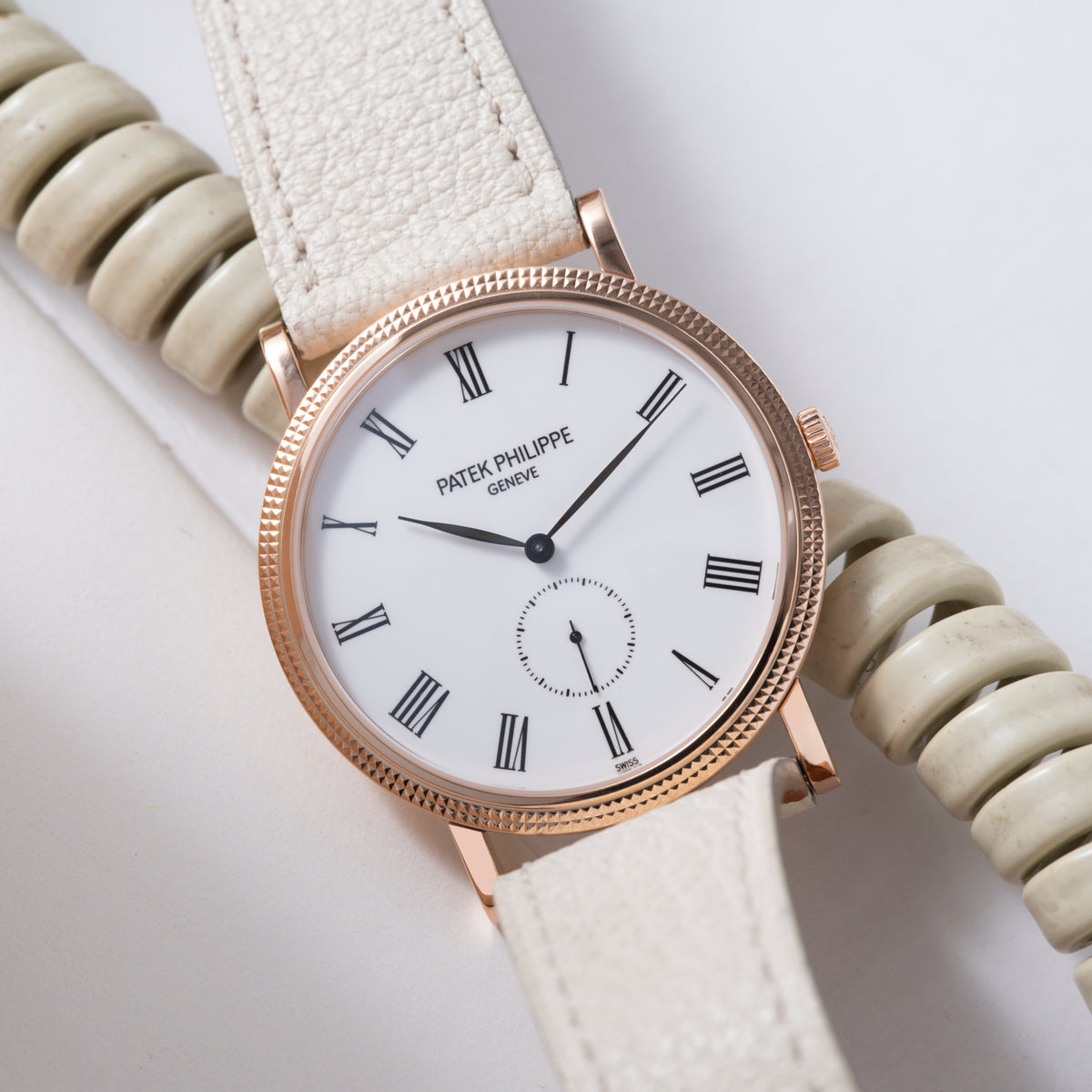 Rose gold Patek Philippe Calatrava watch with white dial, Roman numerals, and cream leather strap.
