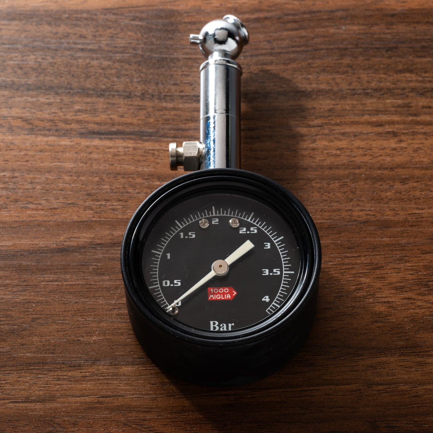 A luxury collectible, the Chopard Mille Miglia Tire Gauge by Chopard features a black dial with bar measurements, a needle at 1.5 bar, and a red center label with white text—all displayed on a wooden surface.