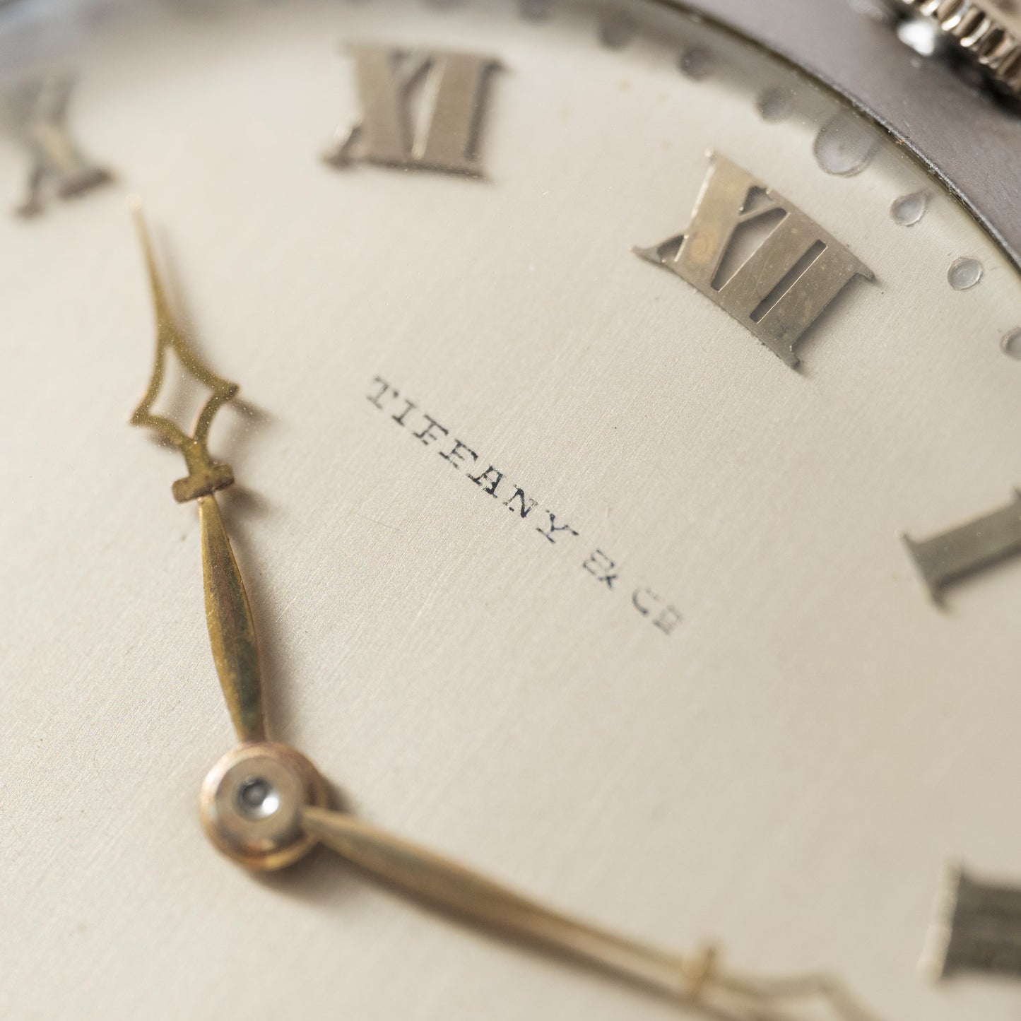 Close-up of a Tiffany & Co. Platinum Pocket Watch face with gold Roman numerals and ornate hands, displaying the time at around 7:52. The Tiffany & Co. brand name is centered on the dial, evoking a classic mechanical style.