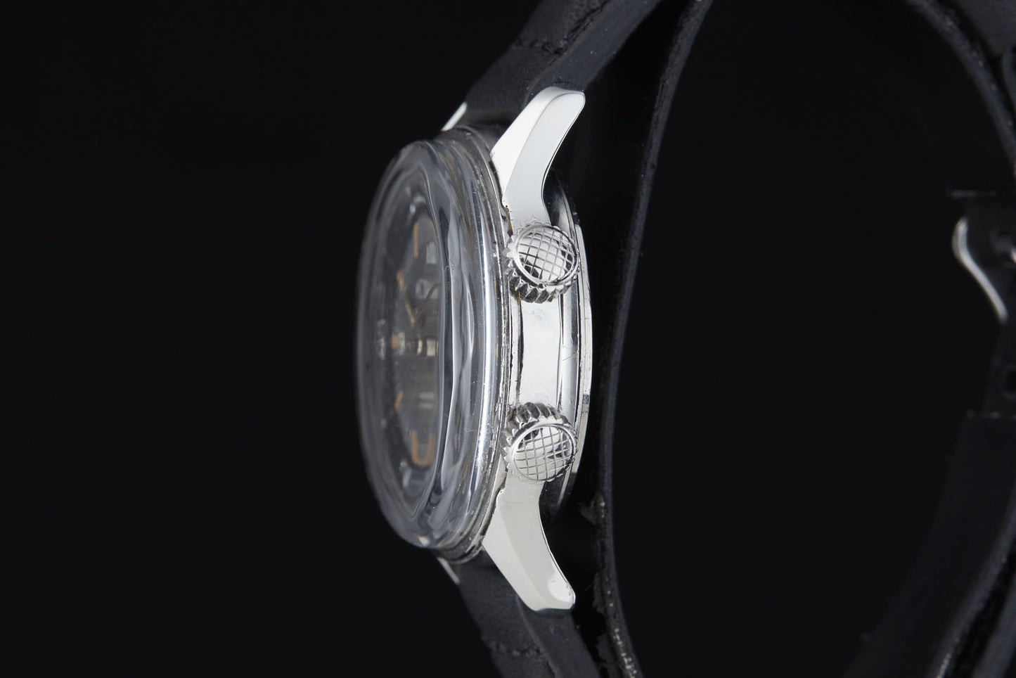 A close-up side view of the Clebar Super Compressor by Clebar, featuring a silver case, two textured crowns like a pressure regulator, and a black strap, set against a plain black background.