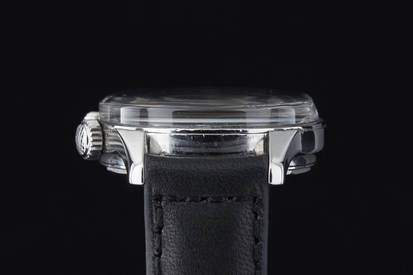The Clebar Super Compressor by Clebar features a thick clear crystal, shiny silver case, and black leather strap—channeling diving suit durability—shown in close-up side view against a black background.