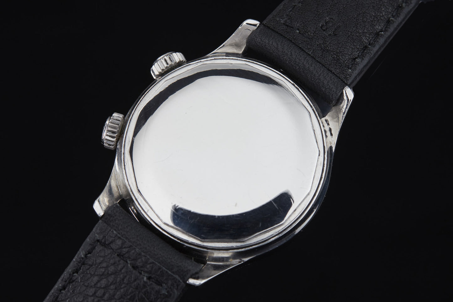 A close-up of the Clebar Super Compressor by Clebar, showcasing its silver case and black leather strap, with two crown buttons reminiscent of a pressure regulator, set against a black background.