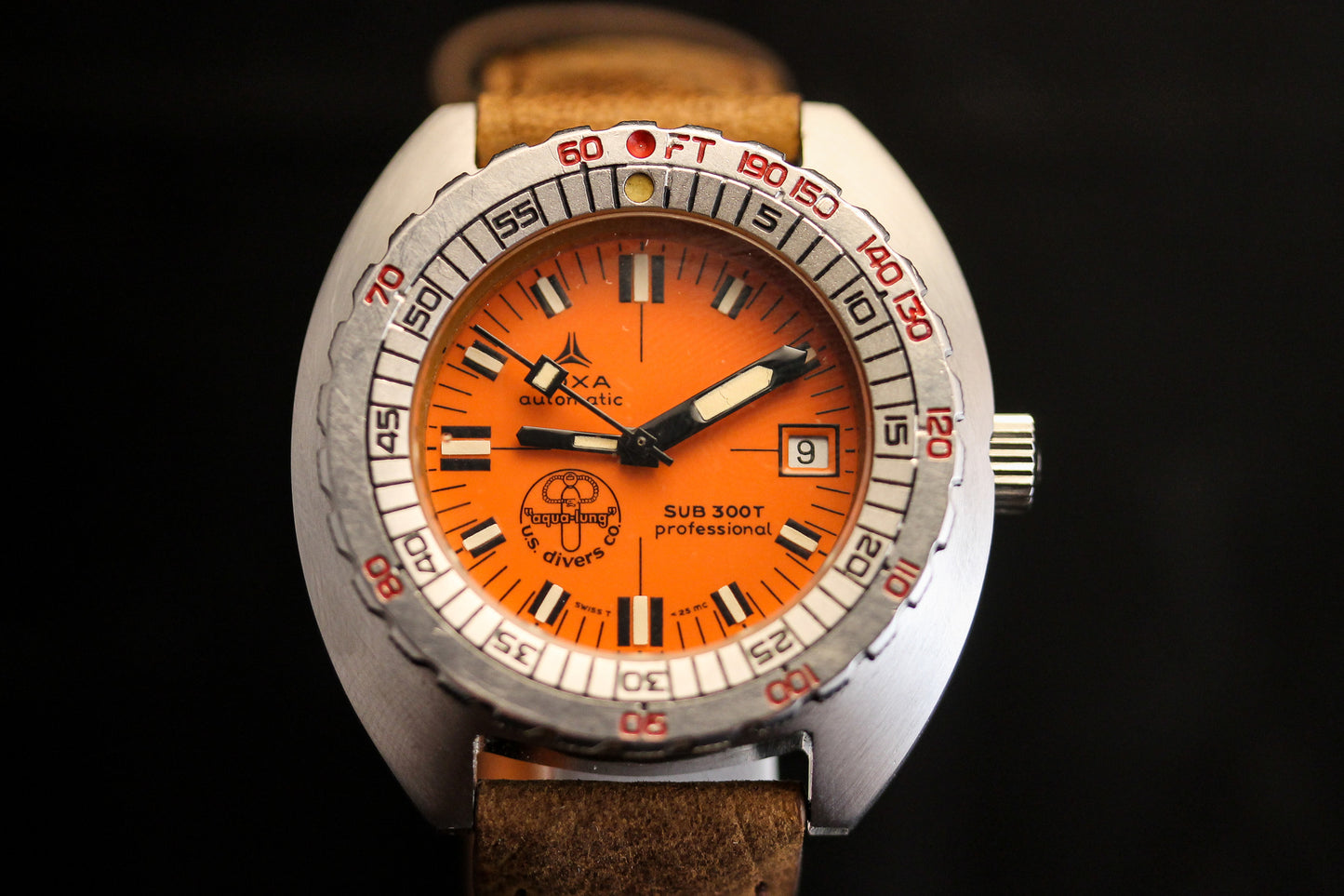 A close-up of the DOXA Sub 300T Professional Aqua Lung shows its orange dial, silver bezel with black and red markers, brown leather strap, and a date window displaying the number 9.