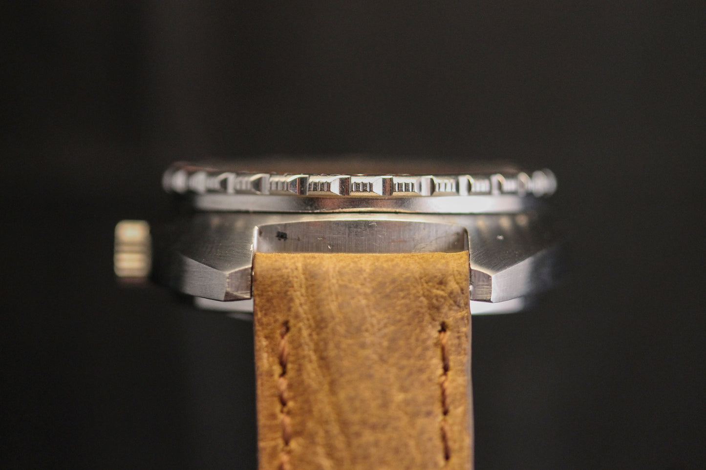 Close-up side view of the DOXA Sub 300T Professional Aqua Lung diver's watch, featuring a metal case, brown leather strap, and signature orange dial. The focus is on the bezel, textured crown, and details against a black background.