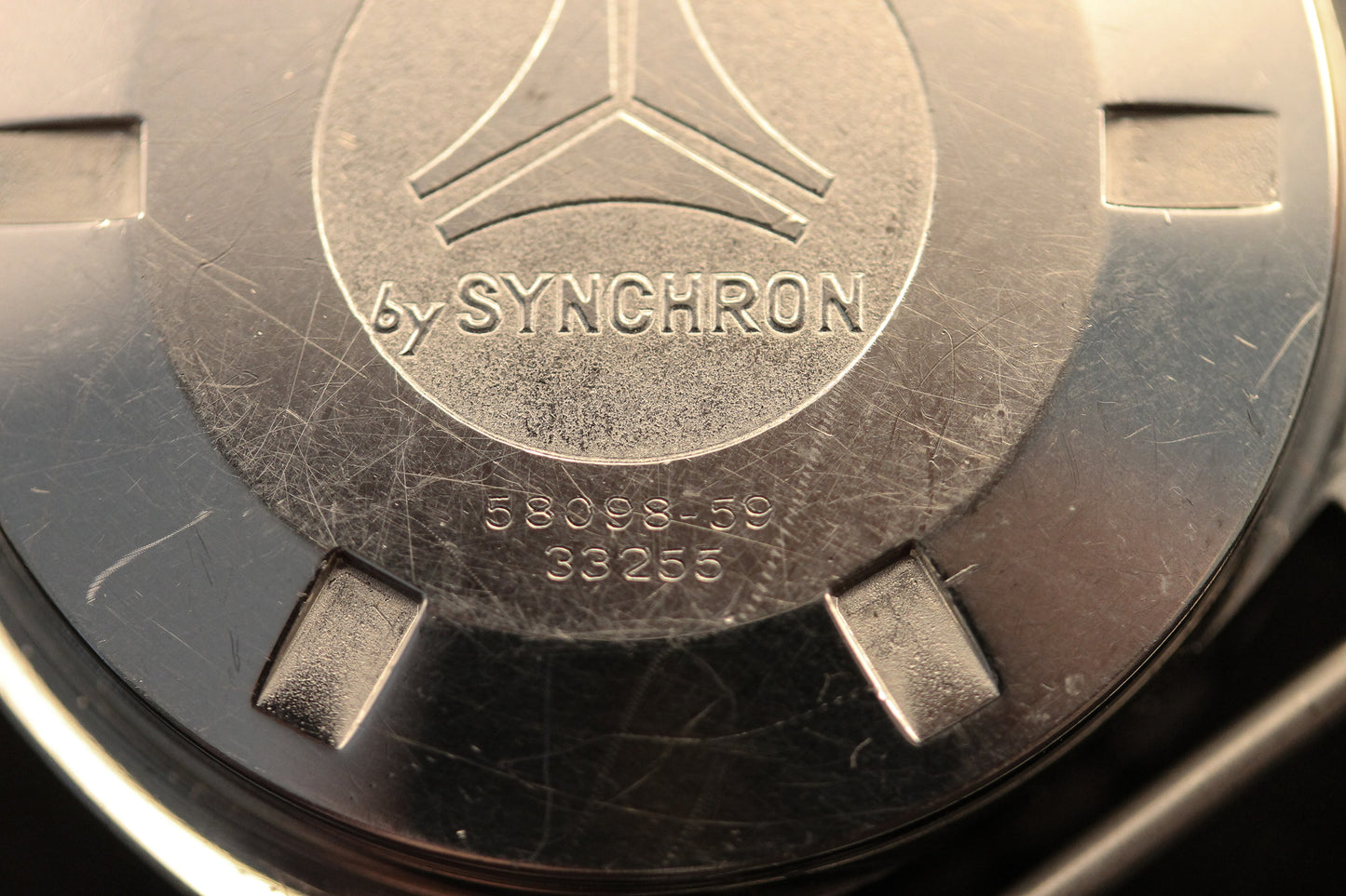 Close-up of the metallic back of a vintage DOXA Sub 300T Sharkhunter, featuring SYNCHRON engraving, numbers 58098-59 and 33255, a geometric logo, and visible surface scratches.