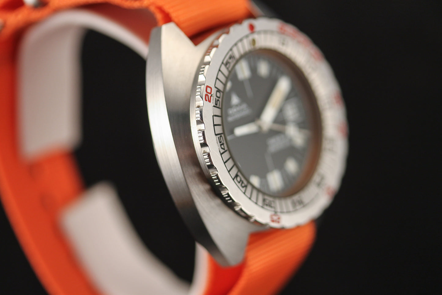 Close-up of the DOXA Sub 300T Sharkhunter diver's watch, featuring a brushed metal bezel, bold white markers on a black dial, orange strap, and precise minute markers—channeling vintage DOXA style against a striking black background.
