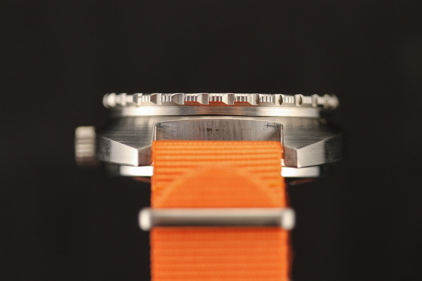 A close-up side view of the DOXA Sub 300T Sharkhunter by DOXA, featuring a silver metal case and bright orange fabric strap, with focus on its crown and bezel against a black background.