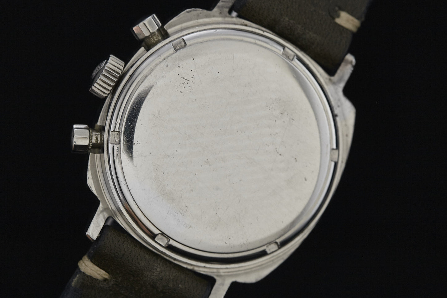 Close-up of the back of a Heuer Camaro stainless steel wristwatch with a black leather strap; the plain caseback shows visible scratches and wear, with two pushers and a crown on the side.