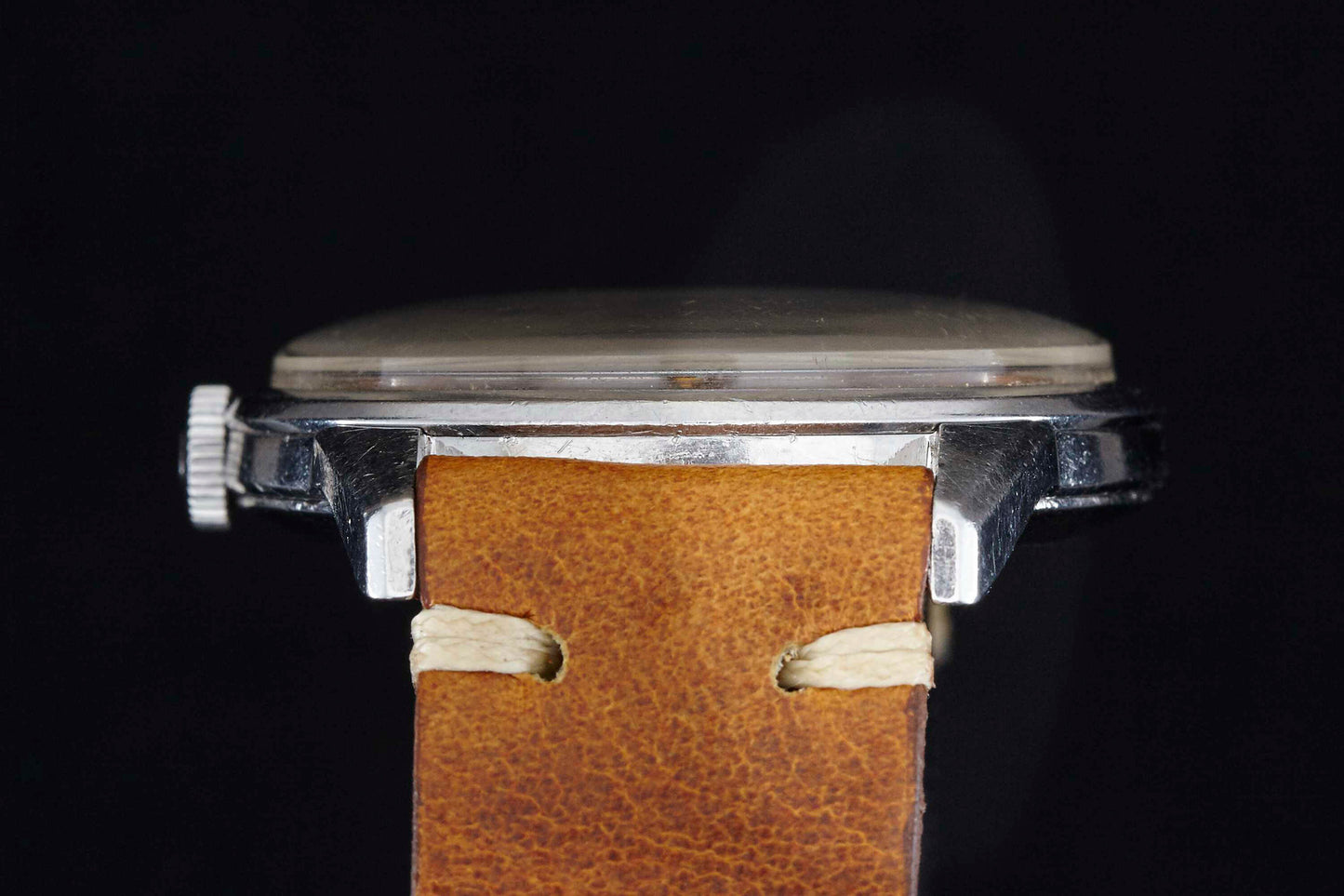 A close-up side view of the Omega Reference 14391-1 vintage watch by Omega, featuring a hand-wound movement, brown leather strap, silver case and crown, set against a black background with the watch face hidden.