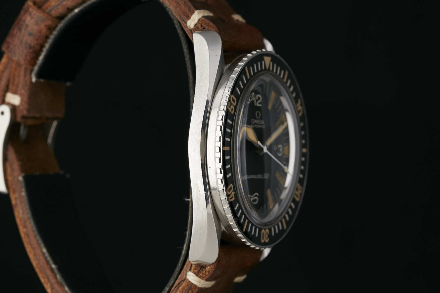 Side view of the Omega Seamaster 300 by Omega, featuring a brown leather strap, silver case, and black dial with white and gold accents. Includes numerals and a rotating bezel against a black background. Detailed description coming soon!.