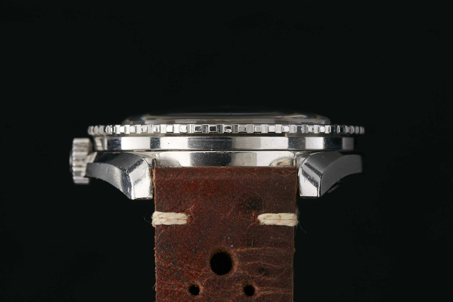 Close-up side view of the Omega Seamaster 300 by Omega, a silver wristwatch with a textured bezel and brown leather strap with visible stitching, set against a black background. Detailed description coming soon!.
