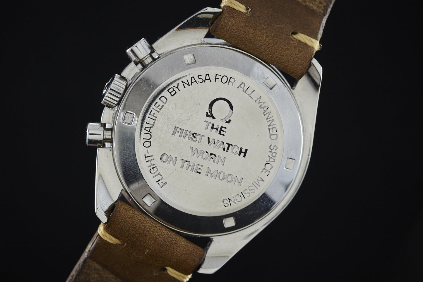 Close-up of the Omega Speedmaster’s back, engraved as the first watch worn on the moon and flight-qualified by NASA for all manned missions. The Omega Speedmaster shown features a brown leather strap.