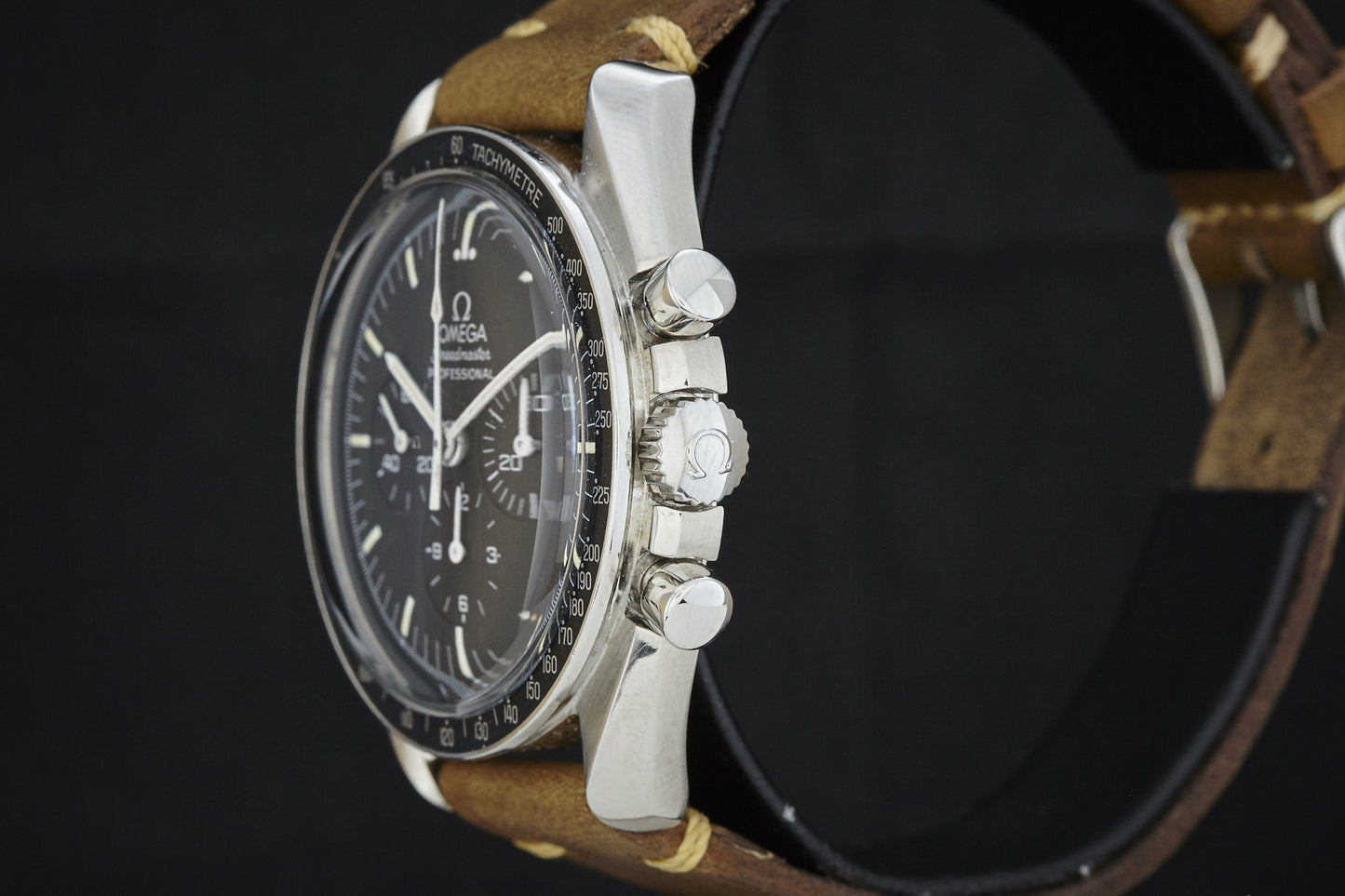 A close-up side view of the Omega Speedmaster by Omega, featuring a black dial, chronograph pushers, and a brown leather strap against a black background.