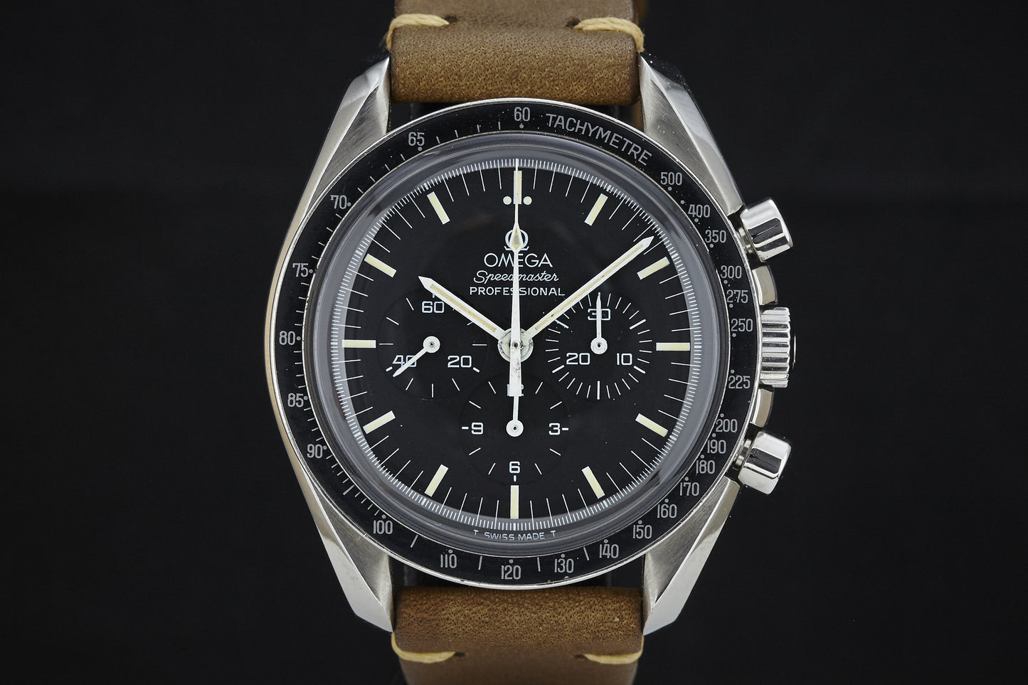 A close-up of the Omega Speedmaster by Omega, featuring a black dial with three subdials, a tachymeter bezel, and a brown leather strap, set against a black background.