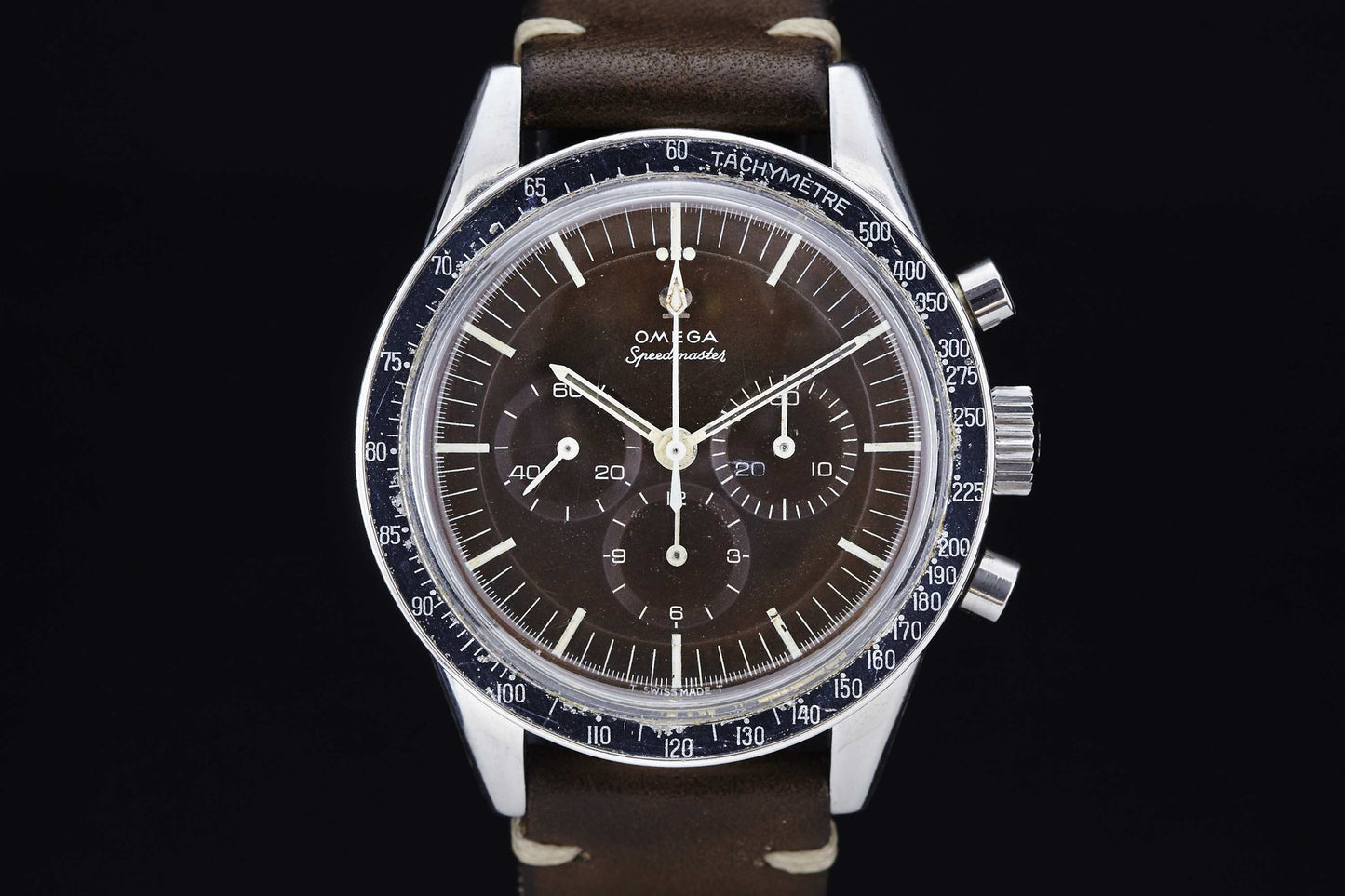 A close-up of an Omega Speedmaster Ed White with a brown dial, three subdials, silver hands, Calibre 321 movement, black tachymeter bezel, and brown leather strap, photographed against a black background.