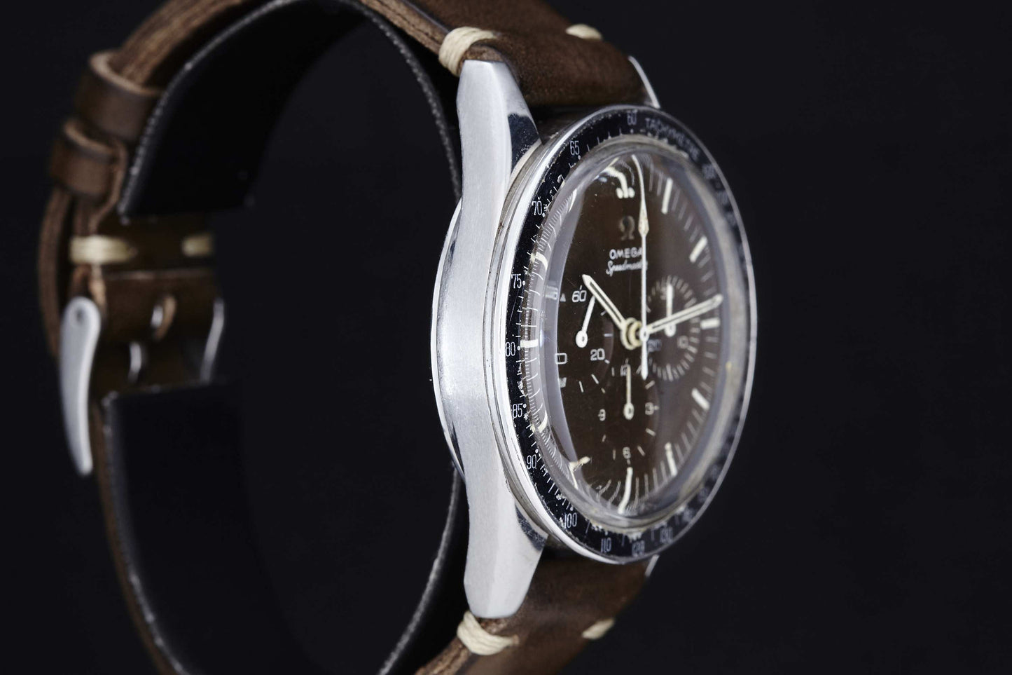 A close-up of the Omega Speedmaster Ed White by Omega, featuring a brown leather strap, silver case, and dark dial with multiple subdials and white markings, set against a black background.