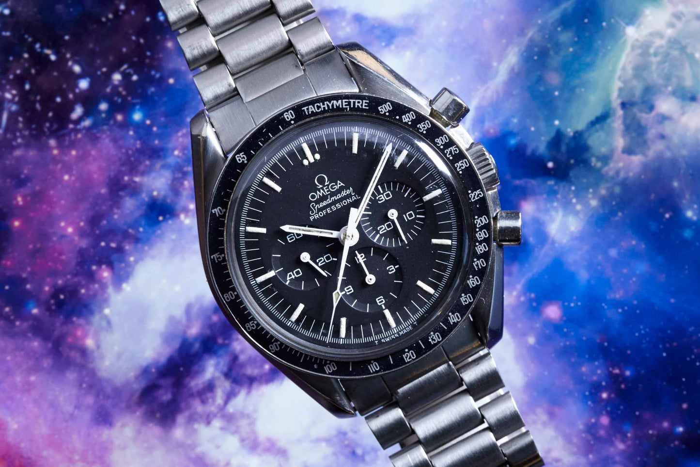 The Omega Speedmaster Professional by Omega, crafted in stainless steel with a black dial and chronograph features, is set against a vivid cosmic background inspired by outer space.