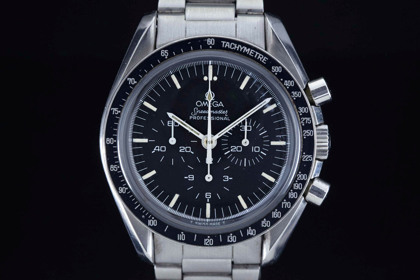 A close-up of the Omega Speedmaster Professional by Omega, featuring a black dial with white markings, three subdials, and a stainless steel case and band against a black background—this legendary watch is NASA approved.