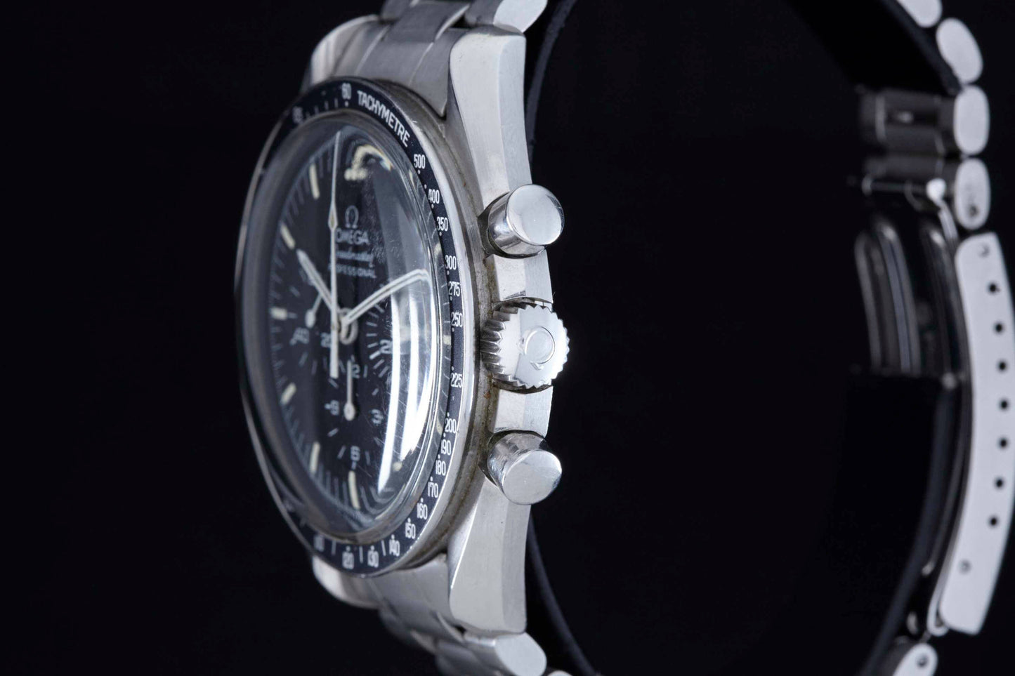 Close-up side view of the Omega Speedmaster Professional by Omega, showcasing its black dial, chronograph buttons, and stainless steel bracelet—famed as NASA's approved watch—all set against a black background.