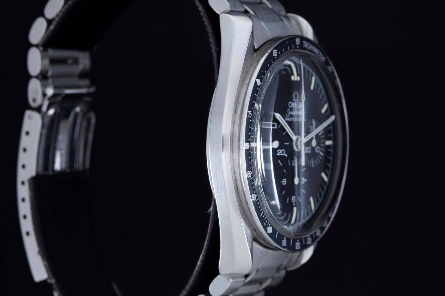 Close-up of the Omega Speedmaster Professional by Omega, featuring a silver case, black dial with white hour markers, and a metal bracelet set against a black background. This iconic moonwatch is NASA approved.