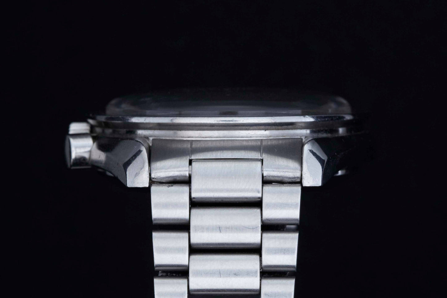 Close-up side view of the Omega Speedmaster Professional by Omega, featuring its linked bracelet and visible crown, set against a black background with part of the iconic NASA-approved moonwatch case in view.