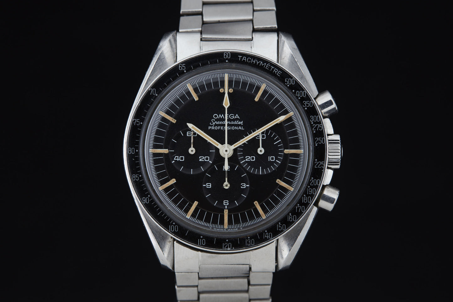 A close-up of the Omega Speedmaster Professional by Omega, featuring a stainless steel band, black dial with three subdials, and tachymeter bezel, set against a black background.