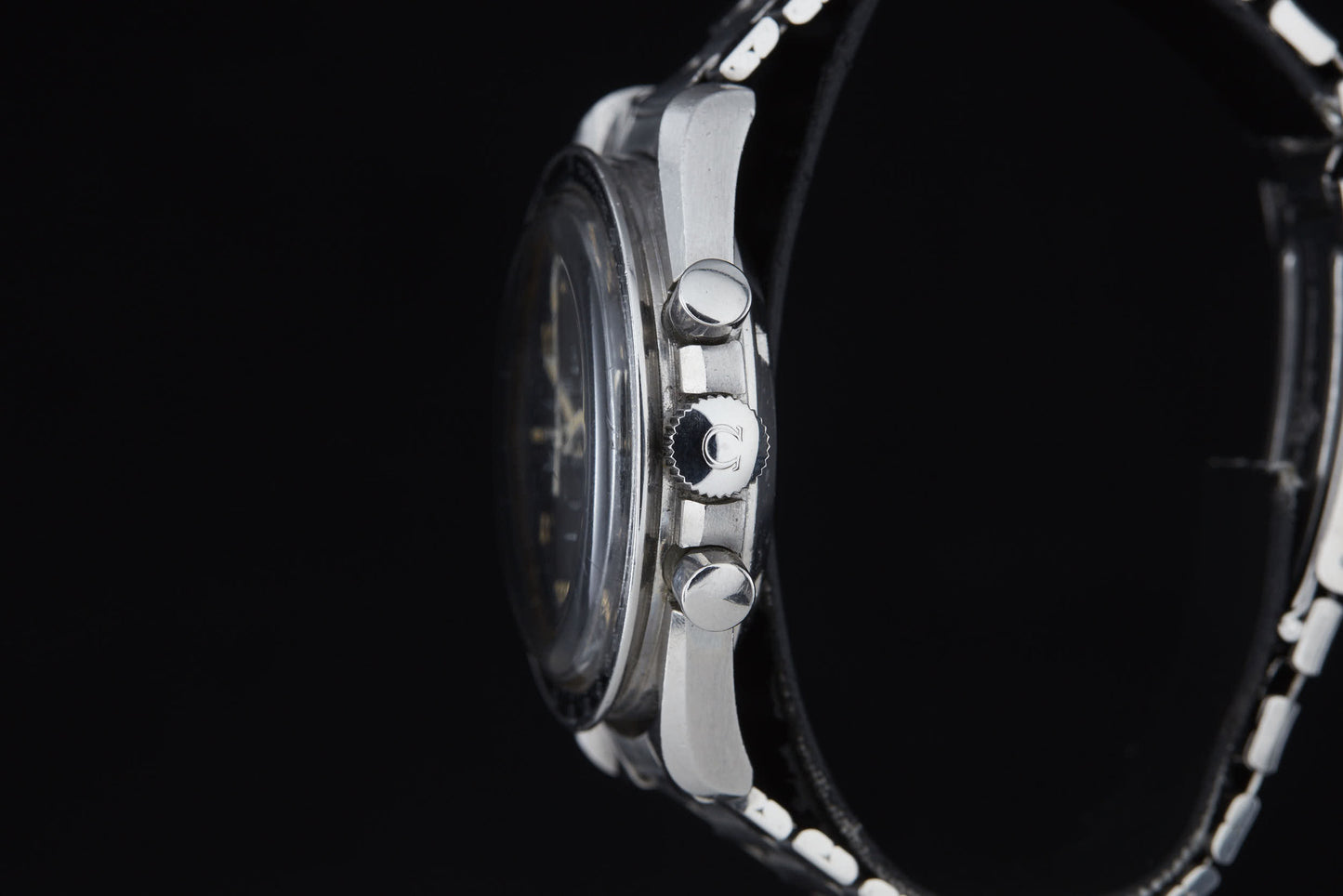 Side view of the Omega Speedmaster Professional by Omega, showing three right-side buttons, a black bezel, and a black and white metal strap against a plain black background—famous for its role in Apollo missions and the moon landing.