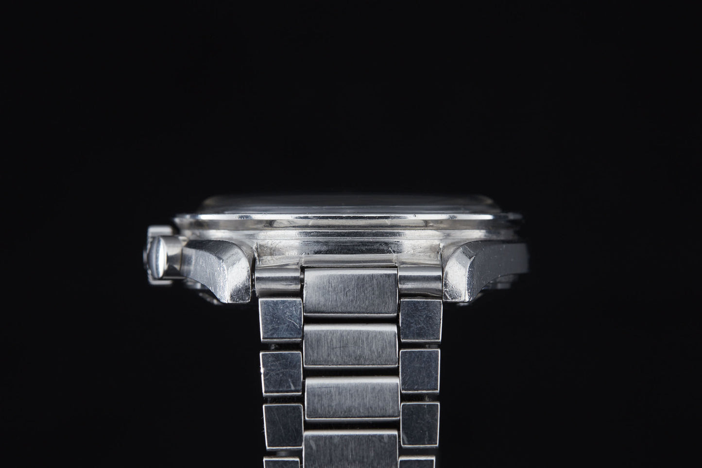 Close-up side view of an Omega Speedmaster Professional by Omega, featuring its detailed case and linked bracelet against a black background; this iconic timepiece was famously worn during the Apollo missions.