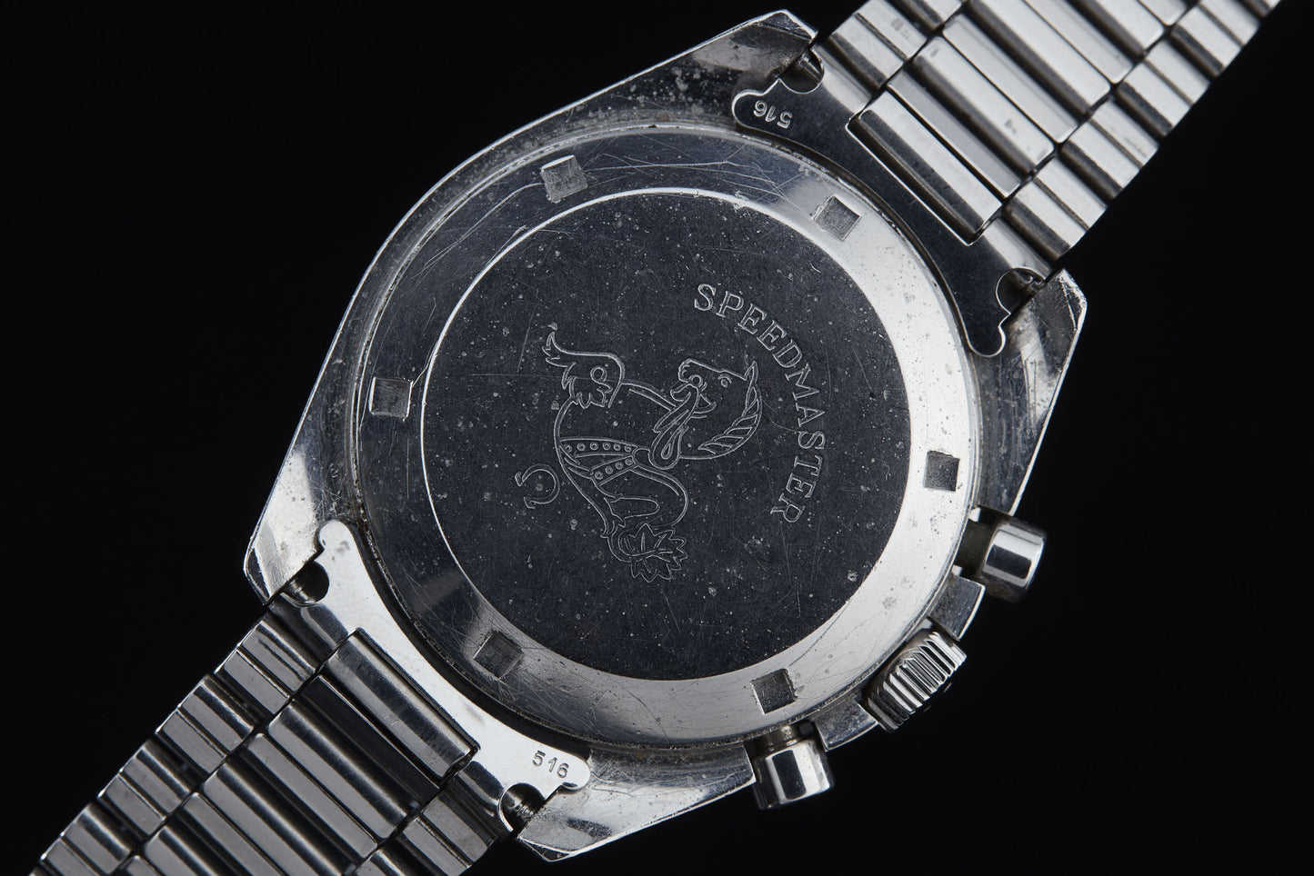 Close-up of the back of an Omega Speedmaster Professional by Omega, featuring the engraved SPEEDMASTER name and seahorse motif. The metal watch band and push buttons are also visible, reflecting its Apollo mission heritage.