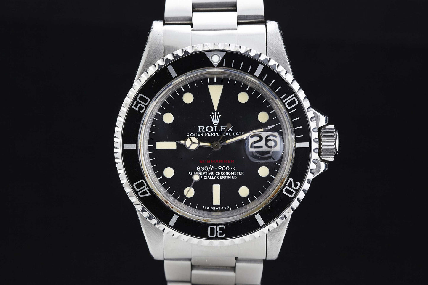 A close-up of the Rolex "Red" Submariner highlights its black dial, white hour markers, rotating bezel, and stainless steel bracelet. The magnified date appears at 3 o’clock on this iconic Rolex dive watch.