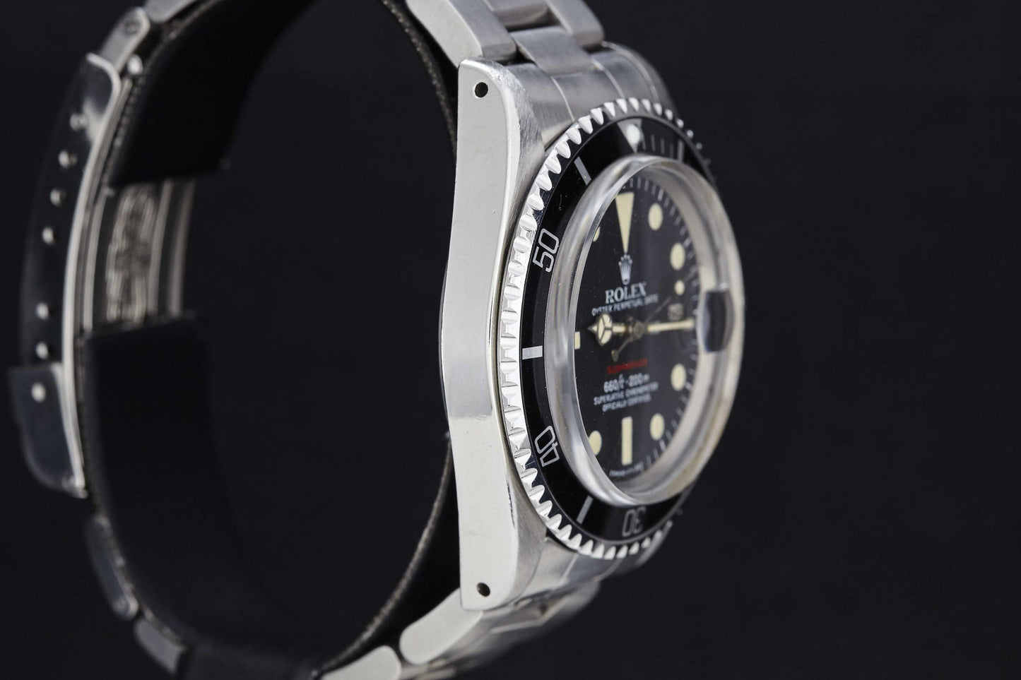 Close-up side view of a Rolex "Red" Submariner dive watch in stainless steel, featuring a black bezel, black dial, and round hour markers against a plain black background. Part of the watchband is visible. Brand: Rolex.