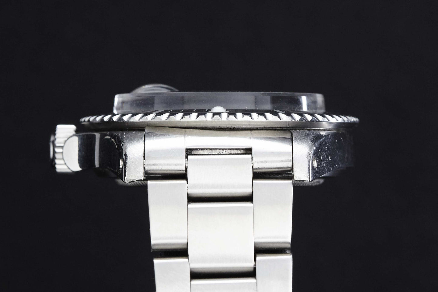 Side view of the Rolex "Red" Submariner dive watch in silver metal, featuring a knurled bezel, left-side crown, and stainless steel link bracelet by Rolex against a black background.