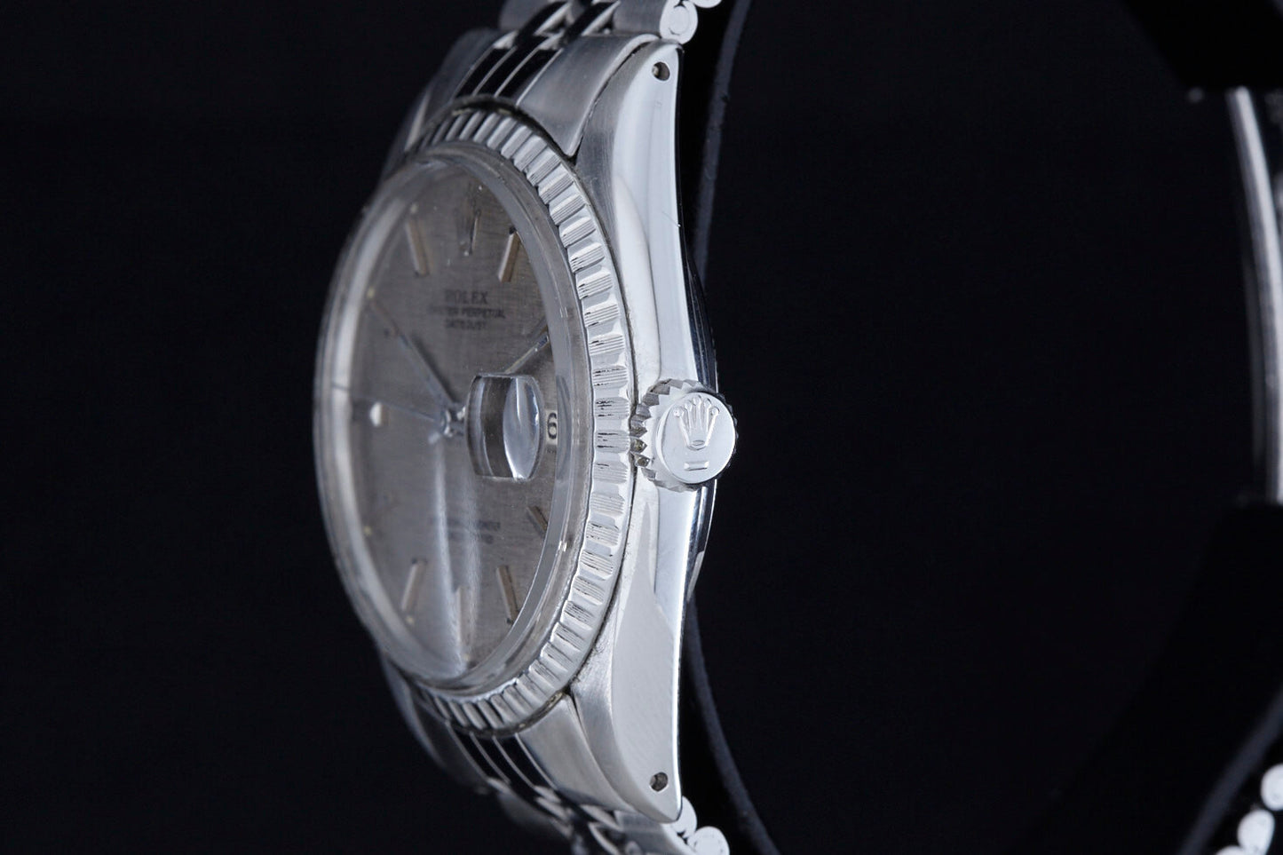 Close-up side view of the Rolex Datejust 1601 Grey Linen, featuring a fluted bezel, grey linen dial, and engraved crown logo on the winding crown, highlighting its automatic movement against a black background.