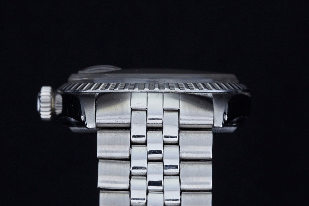 Close-up side view of a Rolex Datejust 1601 Grey Linen wristwatch by Rolex, featuring a metal link band and detailed crown and bezel, set against a black background.