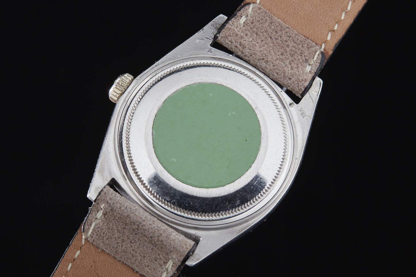A close-up of the back of a Rolex Day Date by Rolex with a leather strap, featuring a green circular sticker on the silver case. The light brown suede-textured strap complements this classic automatic timepiece.