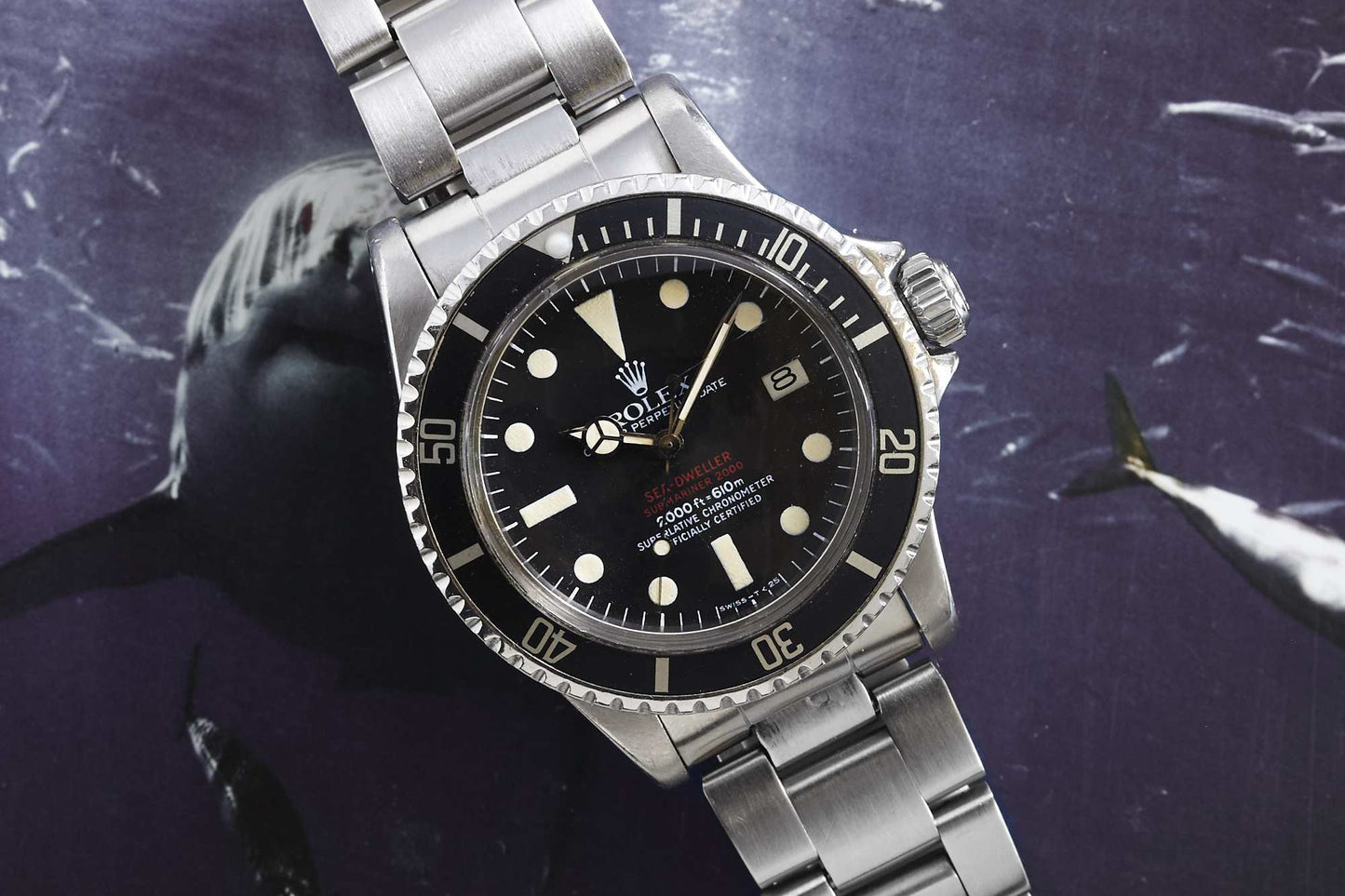 A Rolex Submariner by Rolex with a black dial and bezel, white hour markers, and a metal bracelet rests on a surface covered with swimming seals—a stylish tribute to its Sea Dweller heritage.