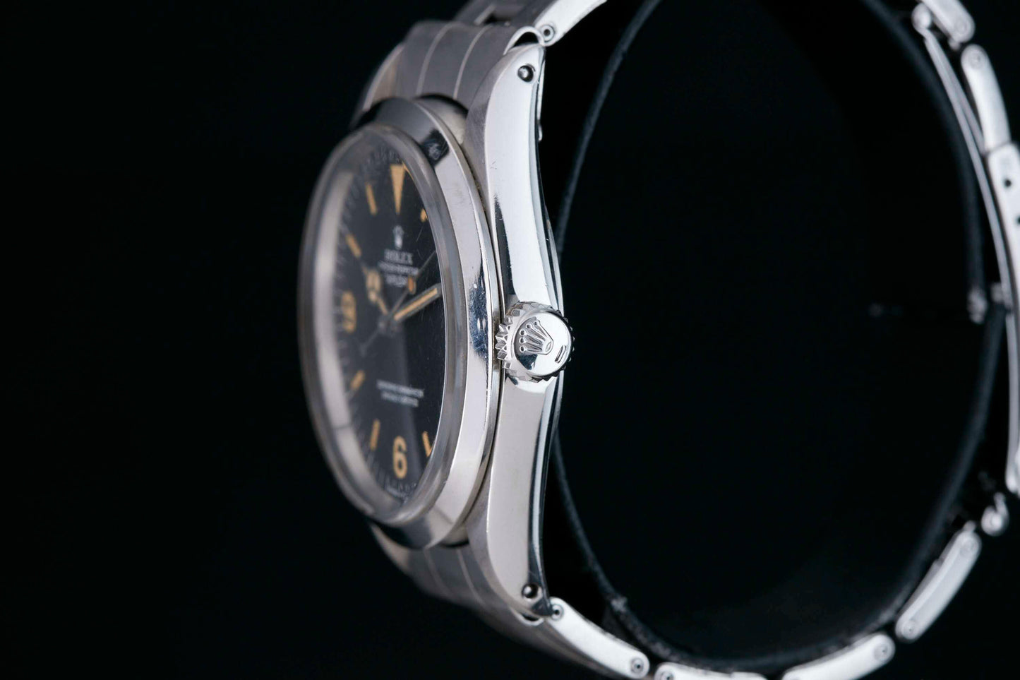 Close-up of a Rolex Explorer by Rolex, featuring a black 3-6-9 Arabic dial. Viewed from the side on a black background, the polished metal case, crown, and part of the strap are visible.