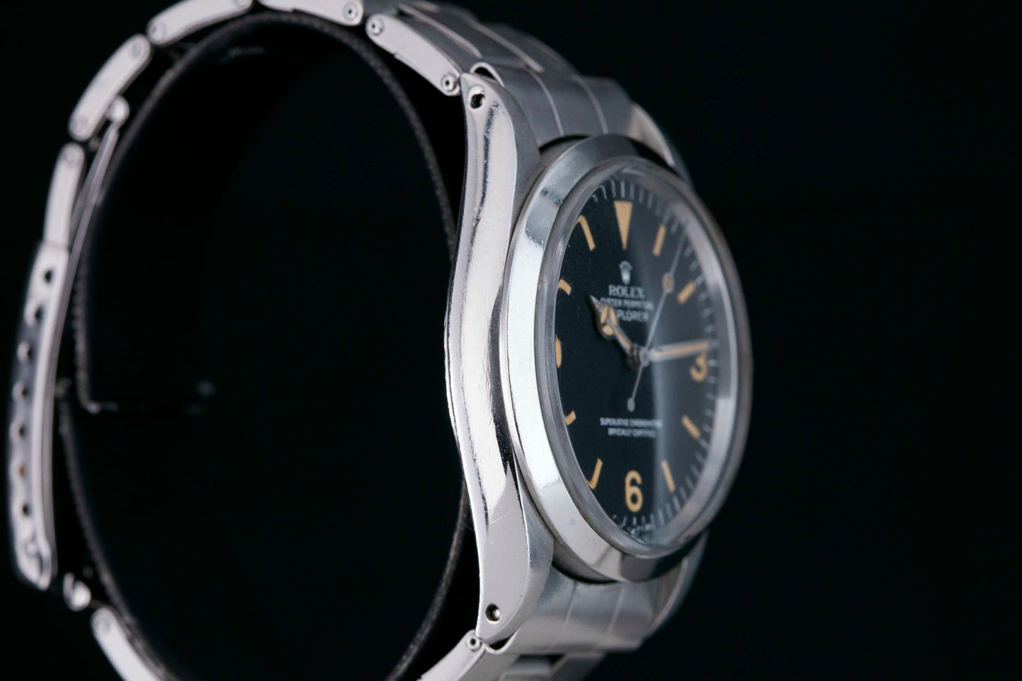 A close-up of a silver Rolex Explorer by Rolex, featuring a black 3-6-9 Arabic dial with orange hour markers, showcased at an angle to highlight its metal band and sleek design against a black background.