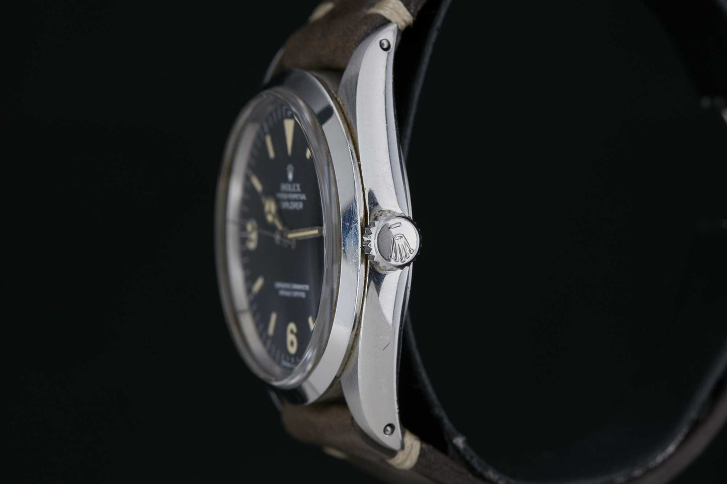 Close-up side view of the Rolex Explorer 1016 featuring a black dial, silver case, and brown leather strap. The Rolex crown logo is visible on the watch crown against a dark background. Detailed description coming soon!.