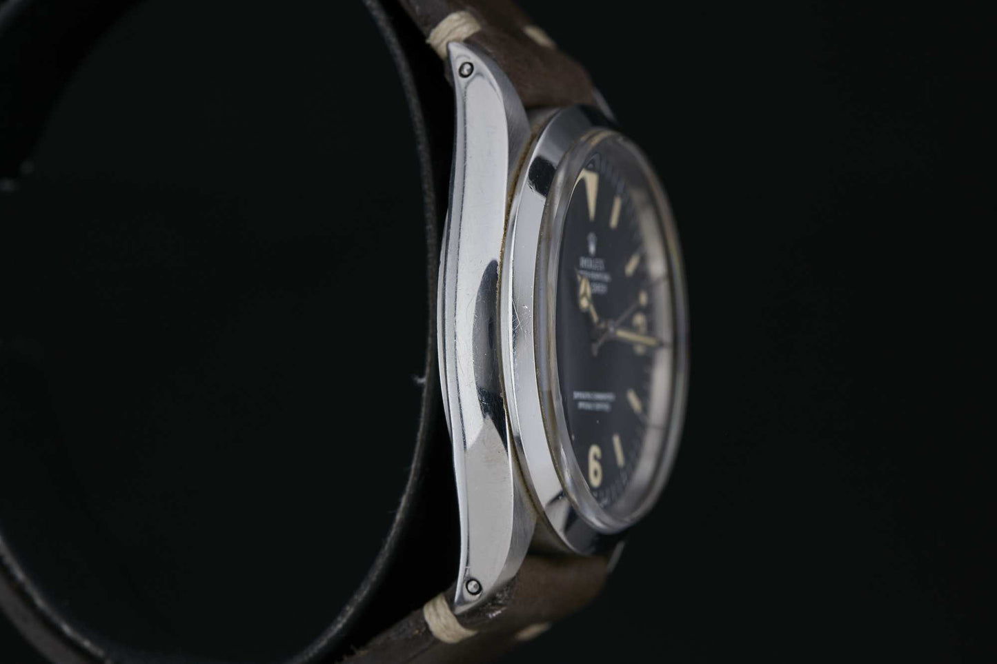 Close-up side view of the Rolex Explorer 1016 by Rolex, featuring a round stainless steel case, dark dial with light indices, and a dark leather strap against a black background. Detailed description coming soon!.