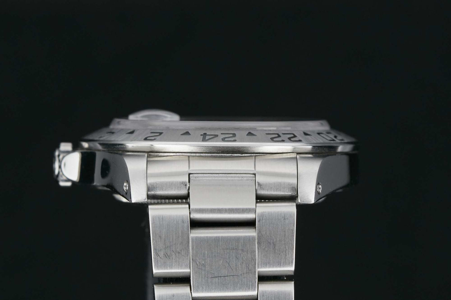 A close-up side view of the Rolex Explorer II by Rolex, featuring a silver metal band, the edge of its watch face, and engraved 24-hour bezel numbers set against a black background.